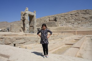 Tourist girl poses in Persepolis in Iran under a blue sky, by Omnimundi