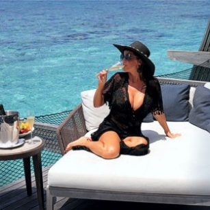 Luxury travel to the Maldives represented here by an elegant woman in swimsuit sitting in a fancy hotel deck