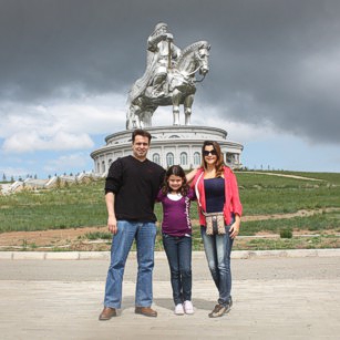 Omnimundi Family of three in Mongolia fields with Ginggis Khaan monument in background