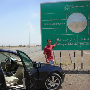 A tourist driving a luxury car in the Oman desert in front of a road sign