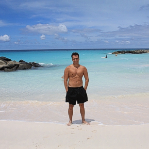 A man standing on a blue waters Beach in Barbados in front of a luxury hotel