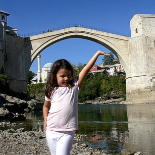 Omnimundi young girl standing under the famous Mostar Bridge in Bosnia