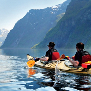 Two adventure sportis in a Kayak paddling inside a beautiful lake with mountains in background