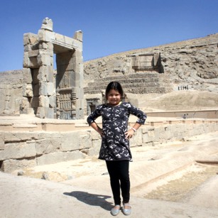 Tourist girl poses near the ruins of Persepolis in Iran under a blue sky, by Omnimundi